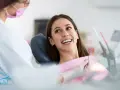 Uśmiechnięta pacjentka podczas wywiadu stomatologicznego. Dentystka w masce przygotowuje się do badania.