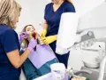 Dentystka z asystentką wykonują zabieg na zębie pacjentki. Dowiadujemy się, jak długo goi się ząb po leczeniu kanałowym.