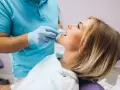 Pacjentka u dentysty, która odczuwa ból szczęki po zabiegu. Dentysta w rękawiczkach bada jej zęby.