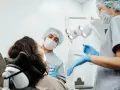 Dentysta przeprowadza leczenie zachowawcze zęba u pacjentki. Asystentka przygotowuje narzędzia.
