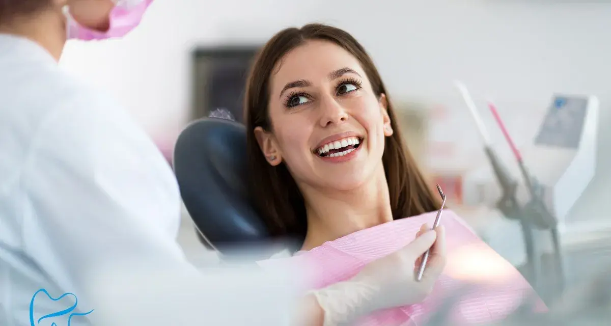 Uśmiechnięta pacjentka podczas wywiadu stomatologicznego. Dentystka w masce przygotowuje się do badania.