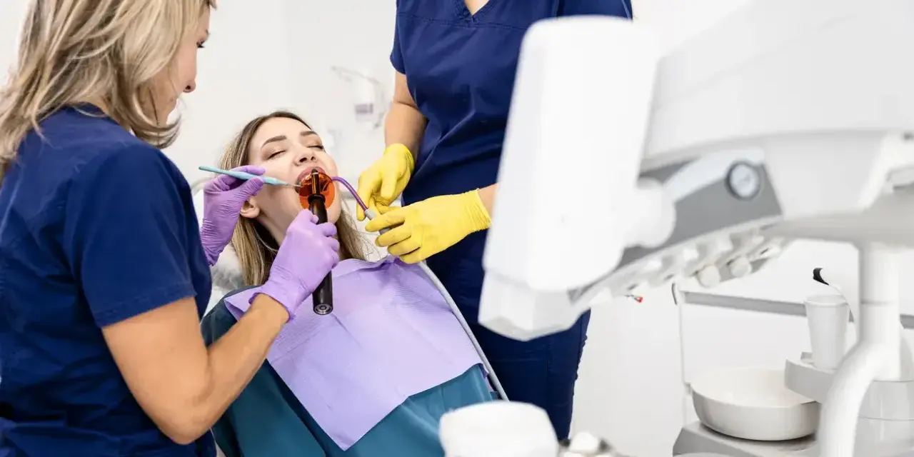 Dentystka z asystentką wykonują zabieg na zębie pacjentki. Dowiadujemy się, jak długo goi się ząb po leczeniu kanałowym.
