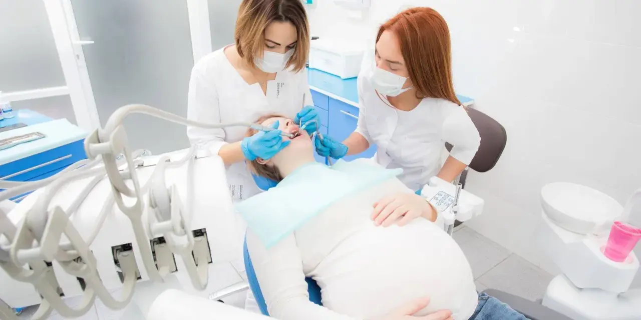 Dentystka leczy zęby ciężarnej pacjentki, dbając o zdrowie jamy ustnej w tym ważnym okresie. Próchnica w ciąży wymaga szczególnej uwagi.