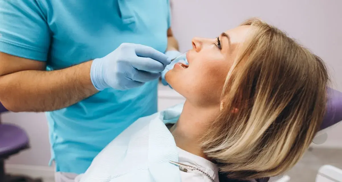 Pacjentka u dentysty, która odczuwa ból szczęki po zabiegu. Dentysta w rękawiczkach bada jej zęby.