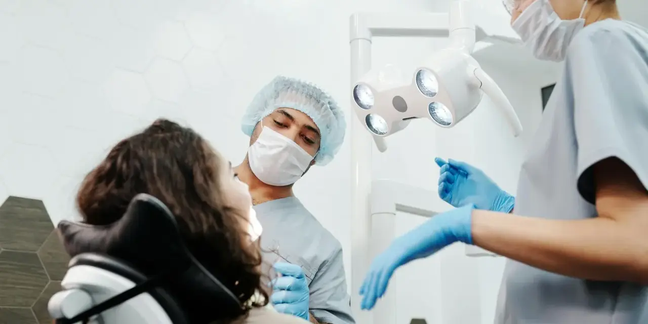 Dentysta przeprowadza leczenie zachowawcze zęba u pacjentki. Asystentka przygotowuje narzędzia.