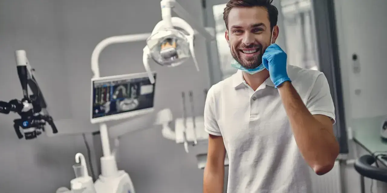 Uśmiechnięty dentysta w gabinecie. Zastanawiasz się, ile trwa plombowanie zęba? Krótka wizyta i piękny uśmiech!