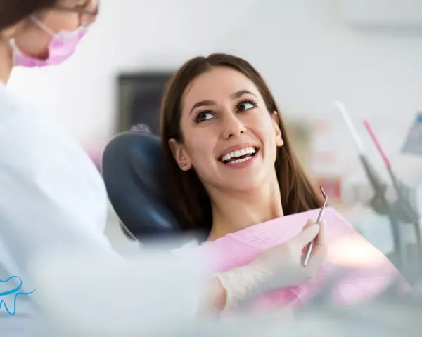 Uśmiechnięta pacjentka podczas wywiadu stomatologicznego. Dentystka w masce przygotowuje się do badania.