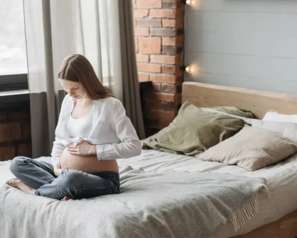 Kobieta w ciąży siedzi na łóżku, delikatnie dotykając brzucha. Może to być związane z nadwrażliwością zębów w ciąży.
