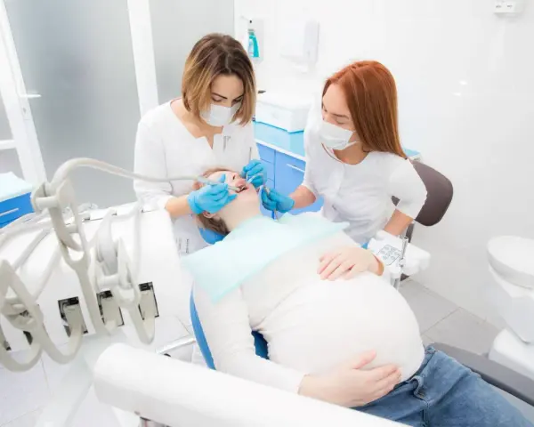 Dentystka leczy zęby ciężarnej pacjentki, dbając o zdrowie jamy ustnej w tym ważnym okresie. Próchnica w ciąży wymaga szczególnej uwagi.