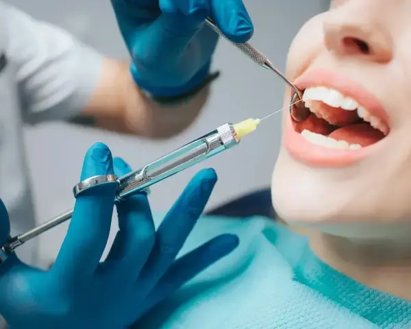 Dentysta podaje znieczulenie. Zamiast domowych sposobów na ruszające się zęby, warto zaufać profesjonalistom.