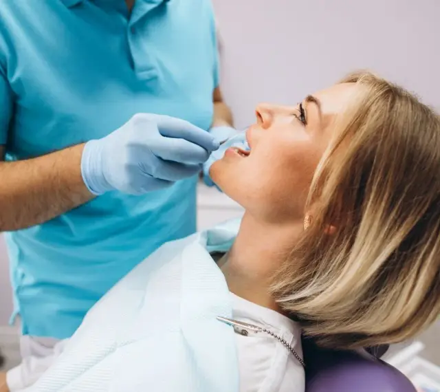 Pacjentka u dentysty, która odczuwa ból szczęki po zabiegu. Dentysta w rękawiczkach bada jej zęby.