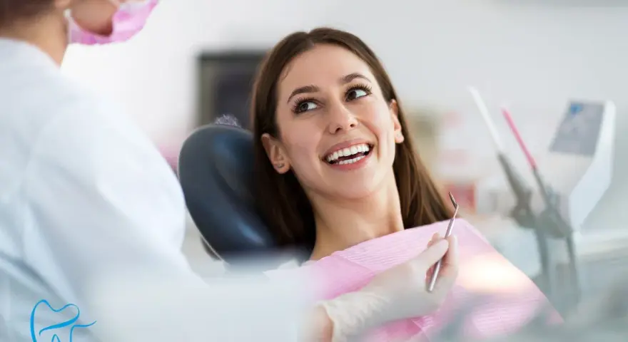 Uśmiechnięta pacjentka podczas wywiadu stomatologicznego. Dentystka w masce przygotowuje się do badania.