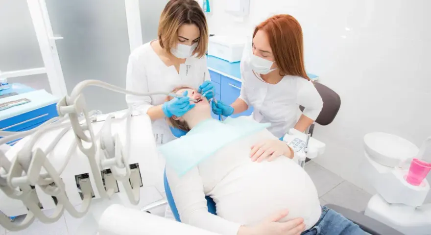 Dentystka leczy zęby ciężarnej pacjentki, dbając o zdrowie jamy ustnej w tym ważnym okresie. Próchnica w ciąży wymaga szczególnej uwagi.