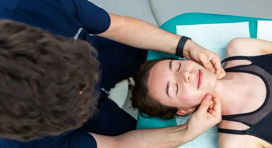 Fizjoterapeuta wykonuje zabieg fizjoterapii stomatologicznej, delikatnie masując twarz pacjentki.