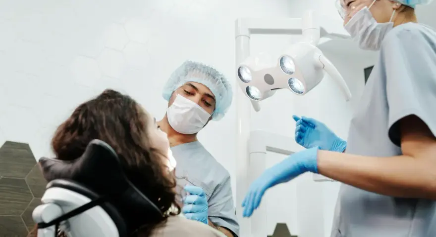 Dentysta przeprowadza leczenie zachowawcze zęba u pacjentki. Asystentka przygotowuje narzędzia.