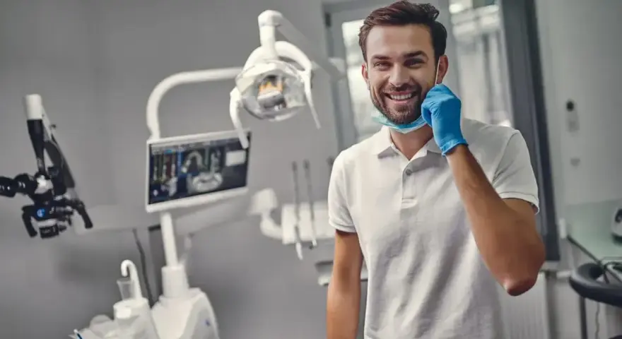 Uśmiechnięty dentysta w gabinecie. Zastanawiasz się, ile trwa plombowanie zęba? Krótka wizyta i piękny uśmiech!