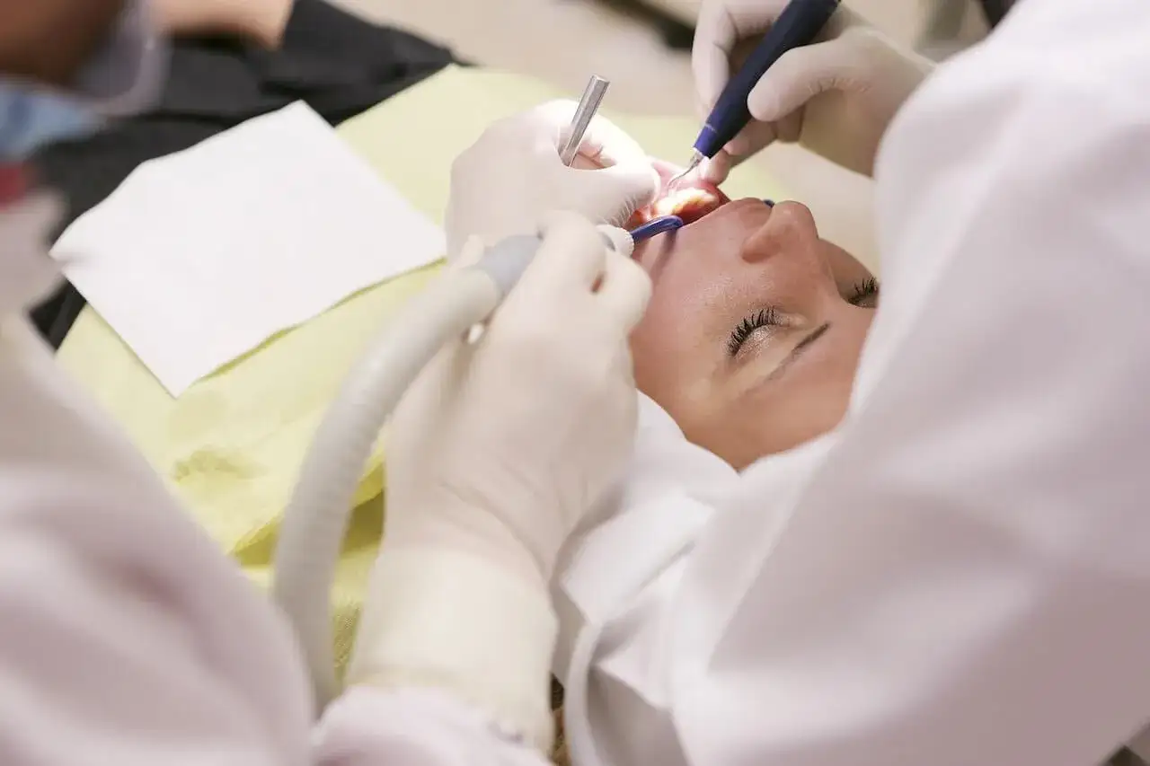Zabieg stomatologiczny: nacięcie ropnia zęba. Dentysta pracuje nad jamą ustną pacjentki, używając narzędzi.