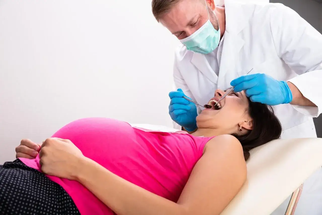 Dentysta bada zęby ciężarnej kobiety, która skarży się na nadwrażliwość zębów w ciąży.