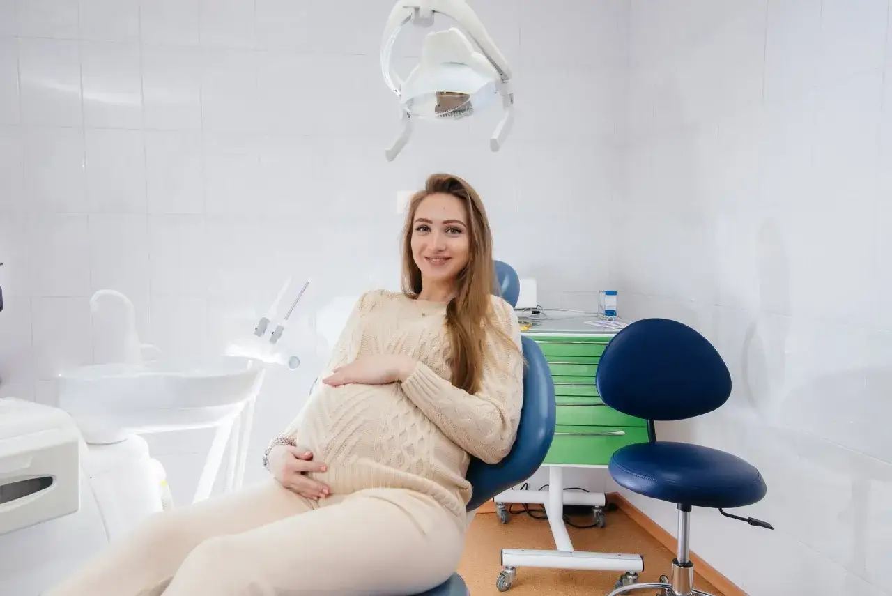Uśmiechnięta ciężarna kobieta w gabinecie stomatologicznym, szukająca odpowiedzi na pytanie: co na ból zęba w ciąży.