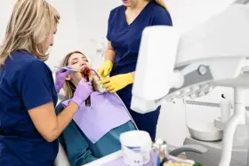 Dentystka z asystentką wykonują zabieg na zębie pacjentki. Dowiadujemy się, jak długo goi się ząb po leczeniu kanałowym.