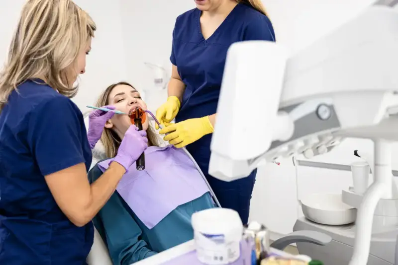 Dentystka z asystentką wykonują zabieg na zębie pacjentki. Dowiadujemy się, jak długo goi się ząb po leczeniu kanałowym.